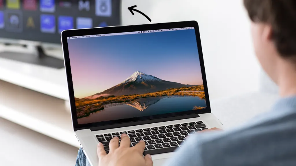 Person holding a MacBook that's connected to a TV monitor